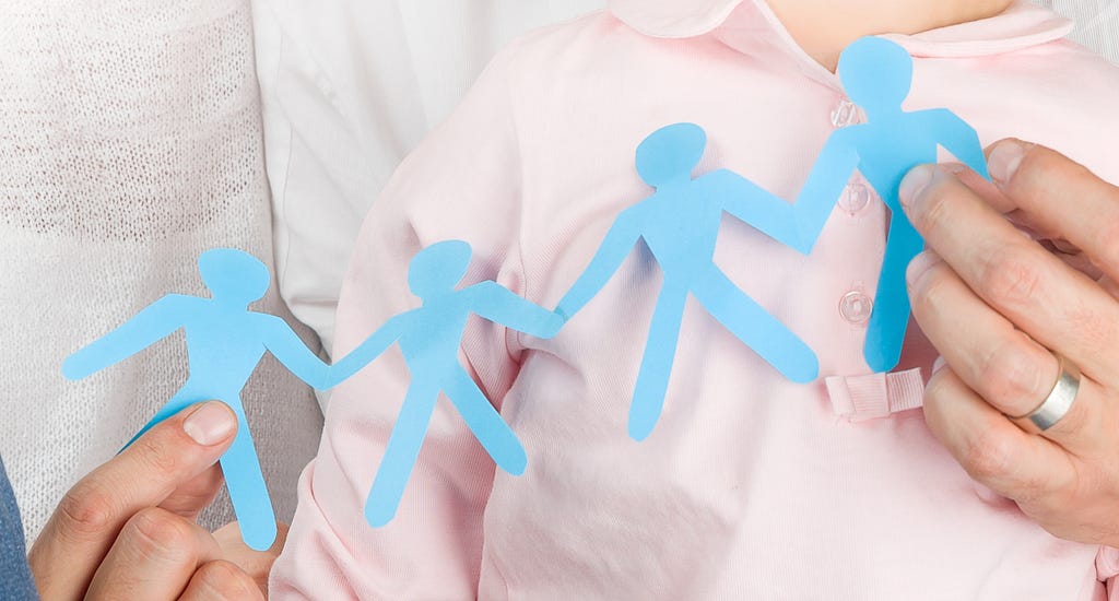 Man's hands holding a blue paper cut group of people.