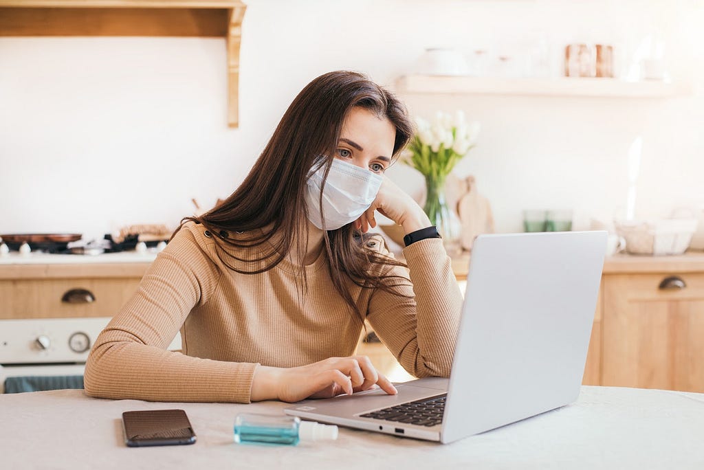 A frustrated young woman working a laptop with facemask