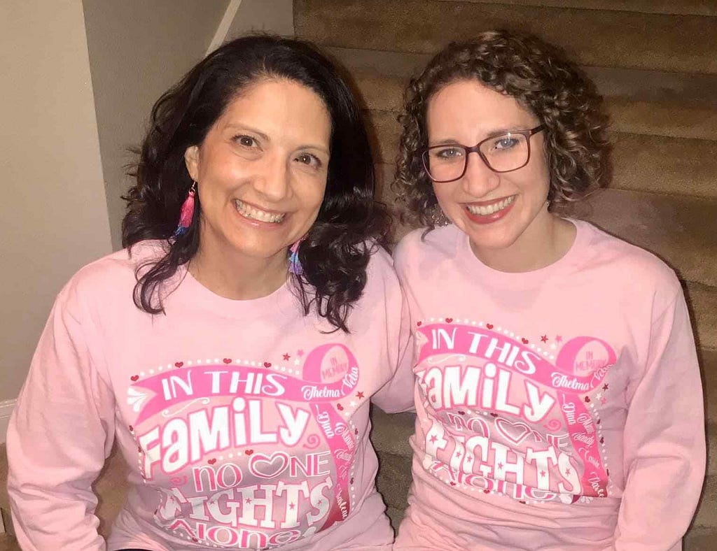 Woman sitting on stairs with her mother, both wearing breast cancer advocate shirts