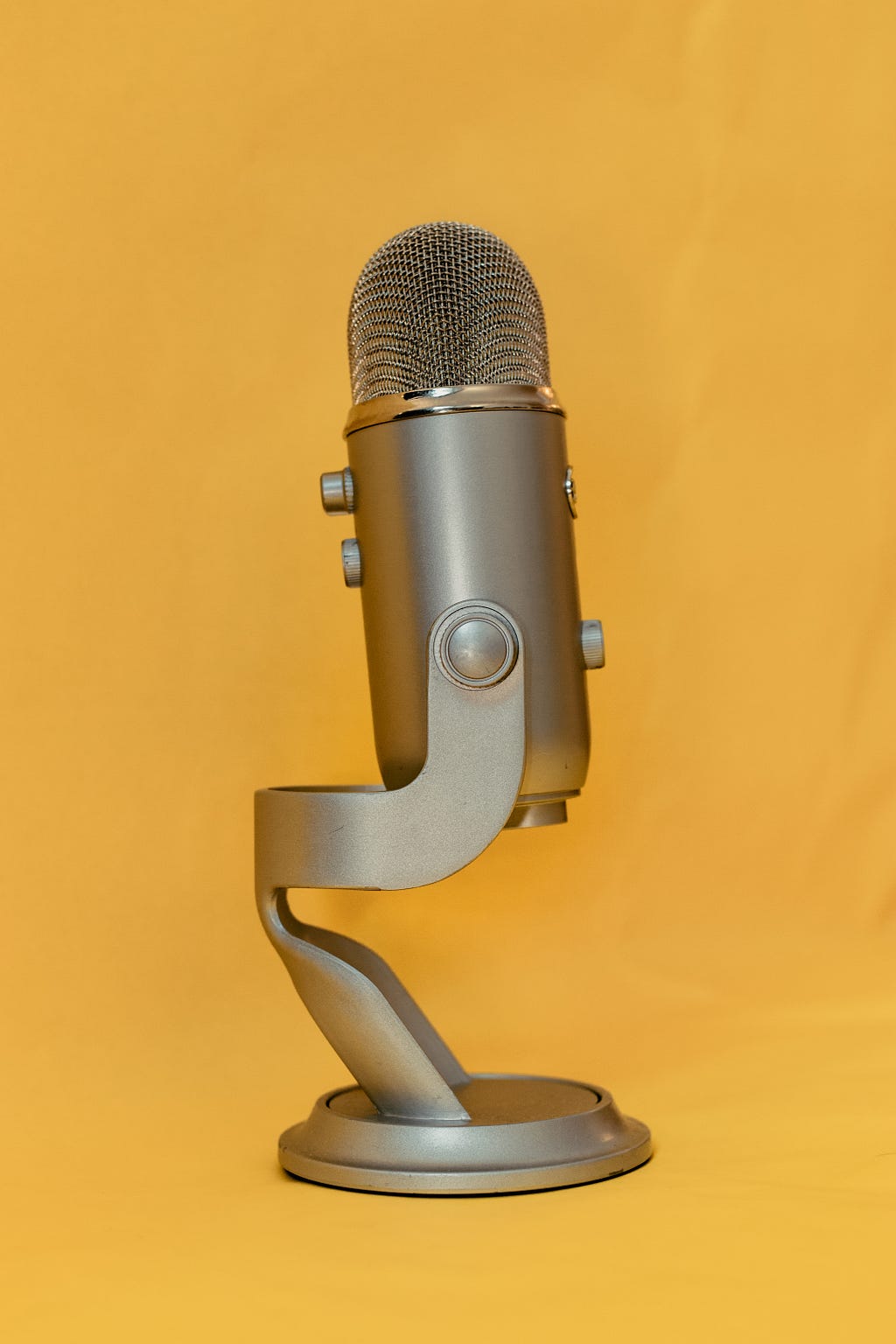 A blue Yeti microphone, silver and standing upright, on a golden yellow background.