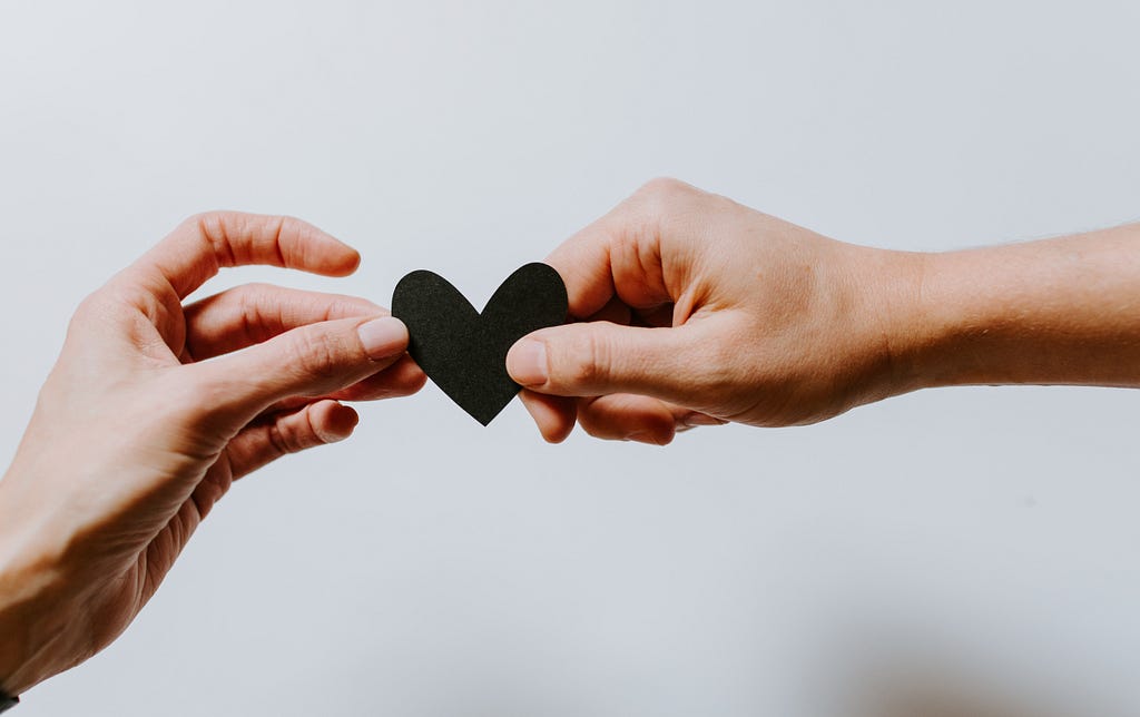 One hand offering a paper heart to another hand