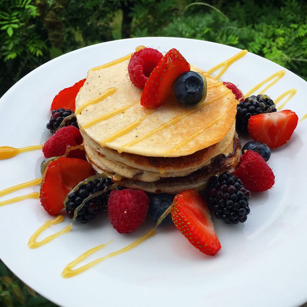 Image of Banana pancakes surrounded by fresh berries and topped with honey