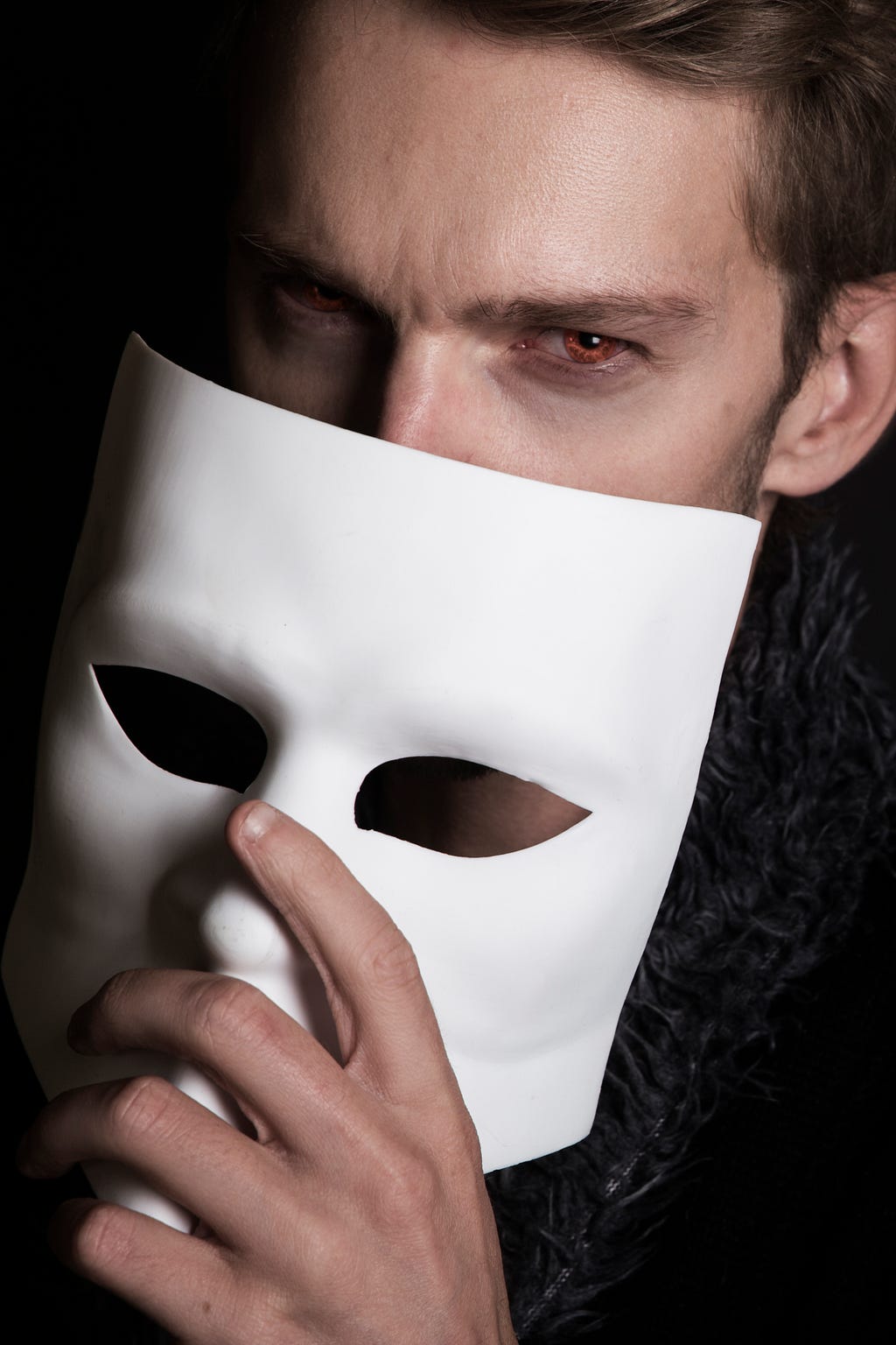 The picture shows a man holding a white mask, to showcase double faced people.