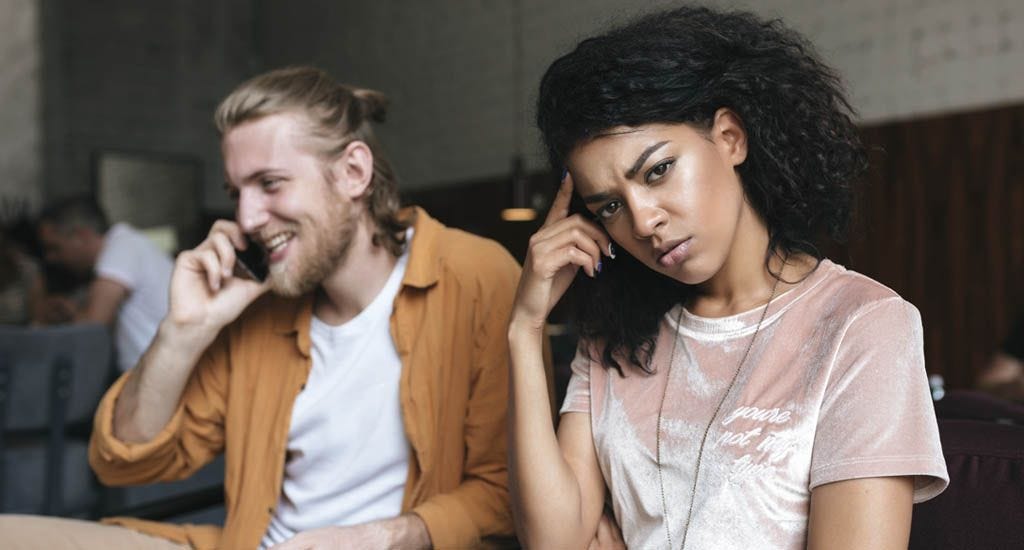 Girlfriend annoyed with her boyfriend talking on his cellphone at cafe