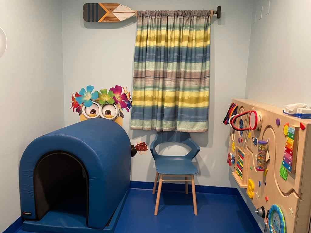 Image depicts a quiet room with a hiding tunnel and activity wall panel. The room is sparsely decorated with a yellow minion on the wall.