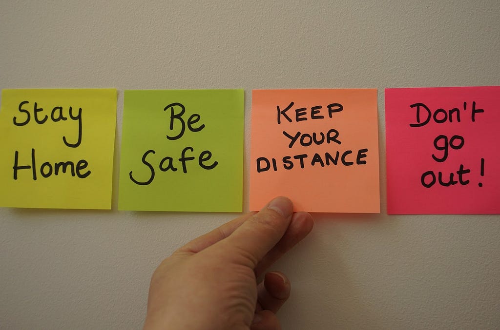 Post-it on a wall saying “stay home, be safe, keep your distance, don’t go out”
