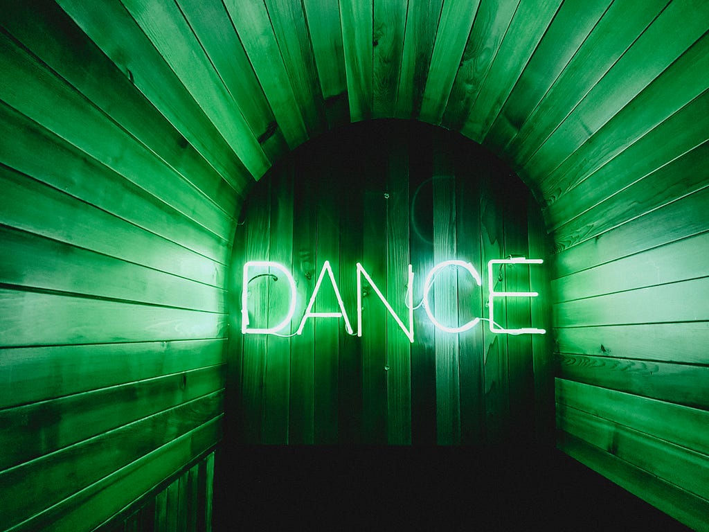 Image of tunnel all in green with the word “DANCE” in the middle of the image in white. Photo by Georgia de Lotz on Unsplash
