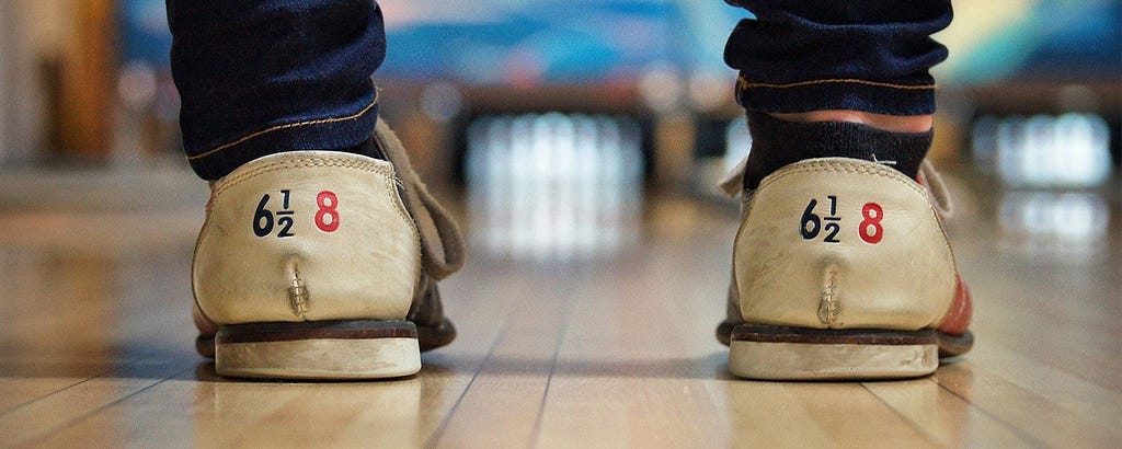 Person in bowling shoes standing at the end of a bowling lane.