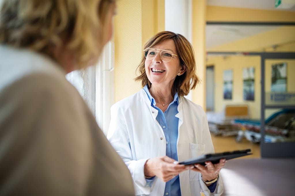 Female doctor referring to her patient’s electronic health record (EHR) while discussing genetic test results with woman