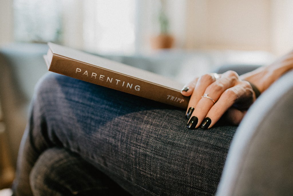 A woman has a book titled Parenting placed on her lap.