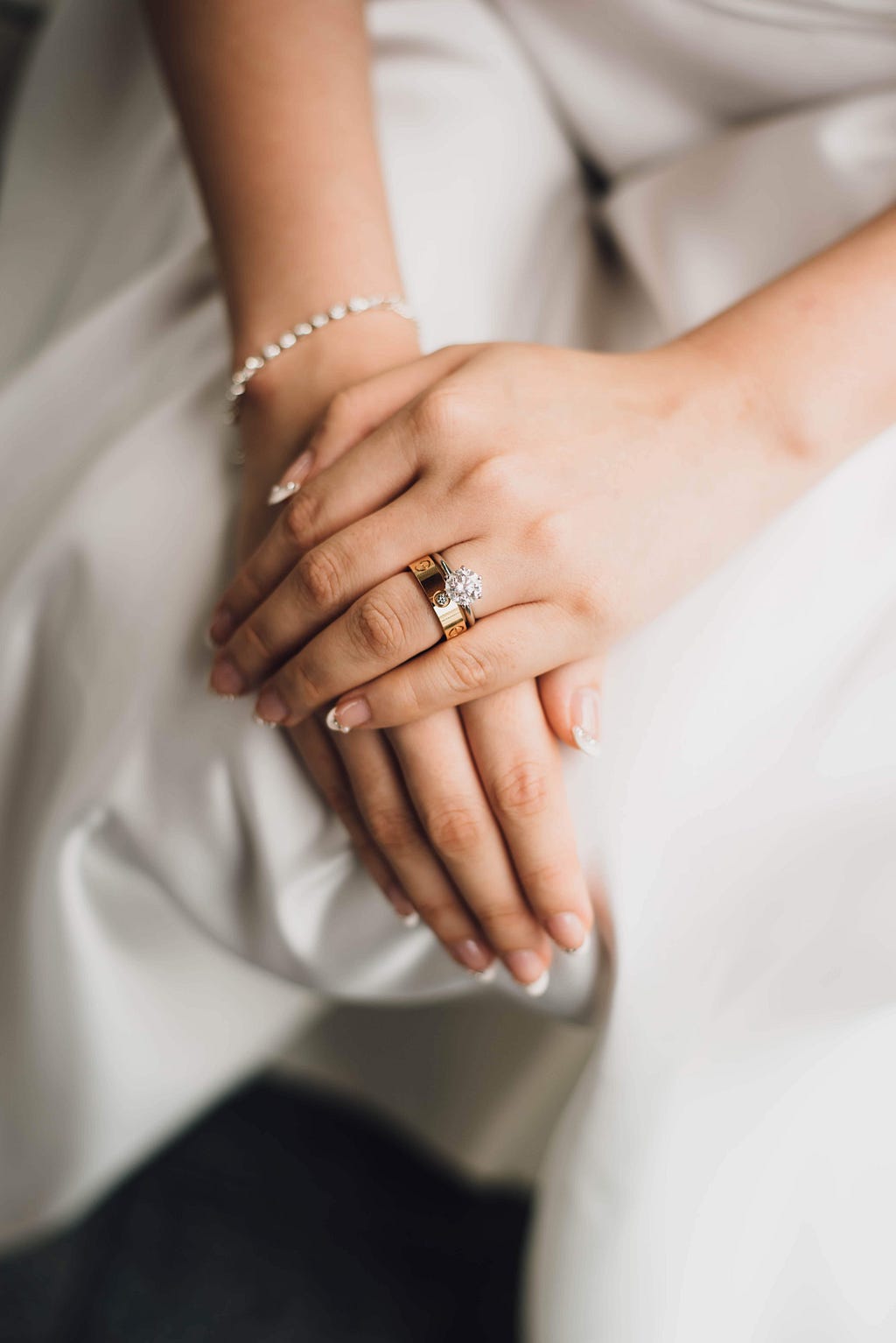 A bride with her hands on her lap showing her engagement ring and wedding band.