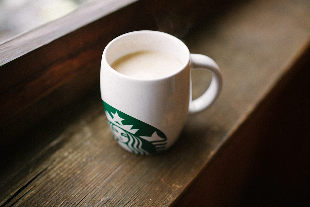 A white Starbucks mug on a wooden window sill.