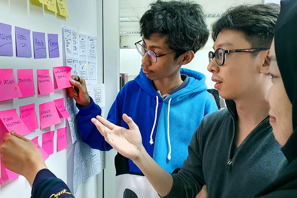 Three UX designers review colourful sticky notes on a whiteboard in an agile way.