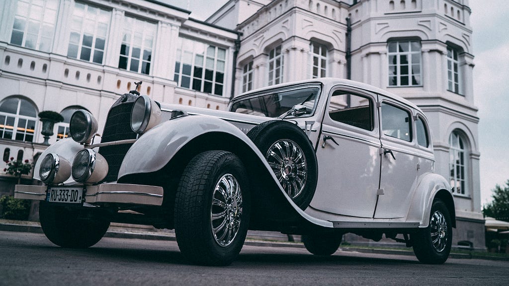 Vintage white Rolls Royce parked in front of a palace