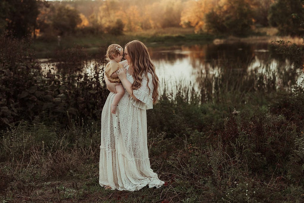 a mom in a long white dress is holding her one year old daugther