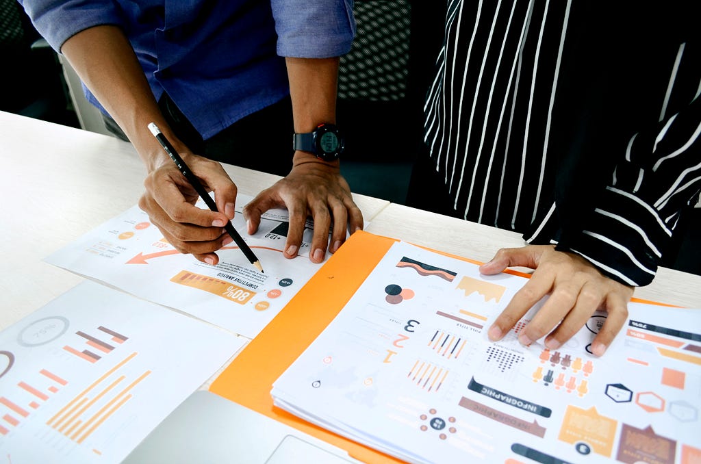 Two pair of hands are writing on pieces of paper that show graphs