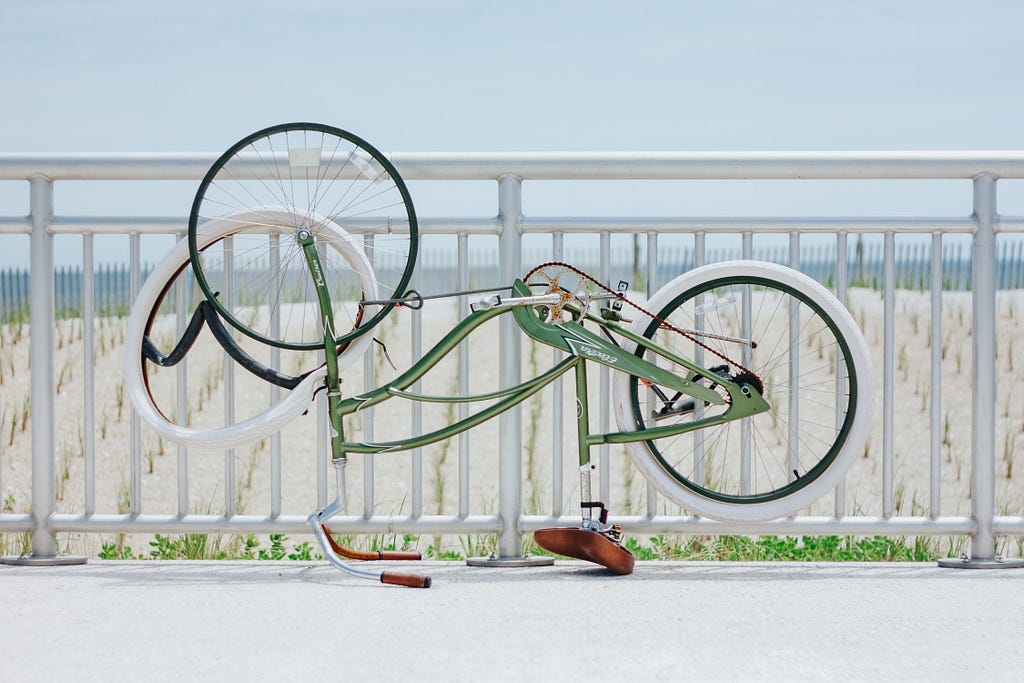 A teal bicycle with white wheels positioned upside down on the ground with the front tire hanging off.