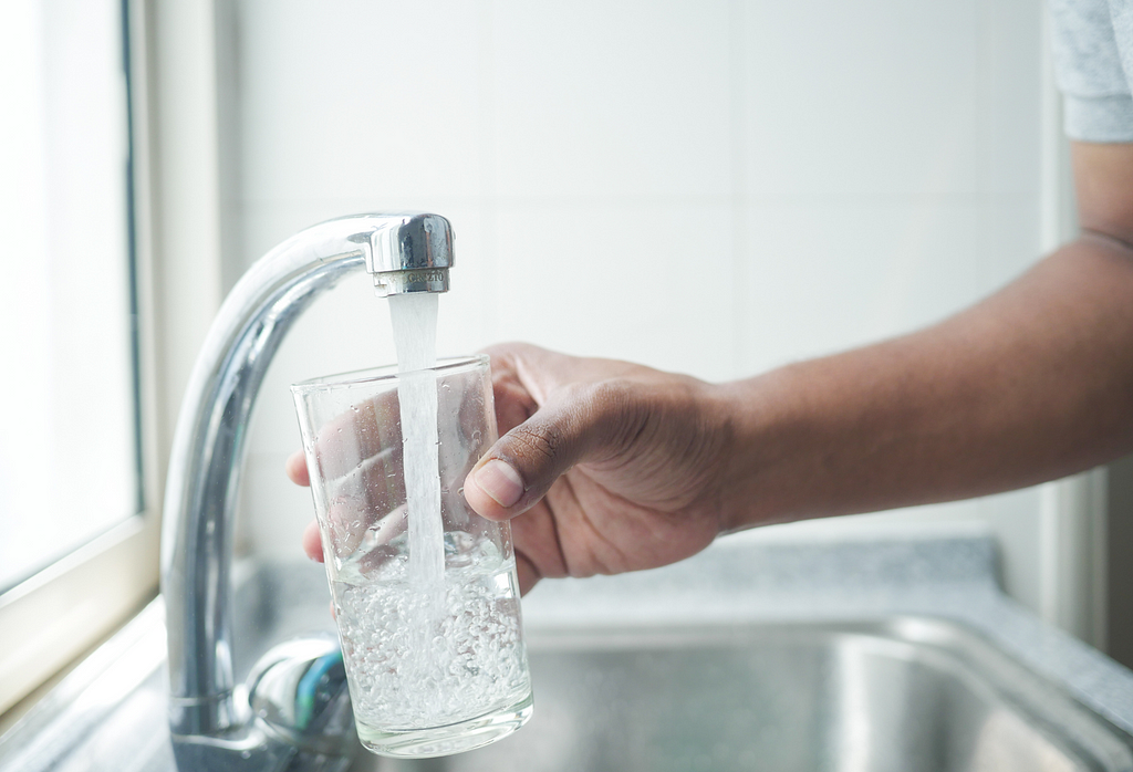 A person is holding a glass getting water from the tap above the sink