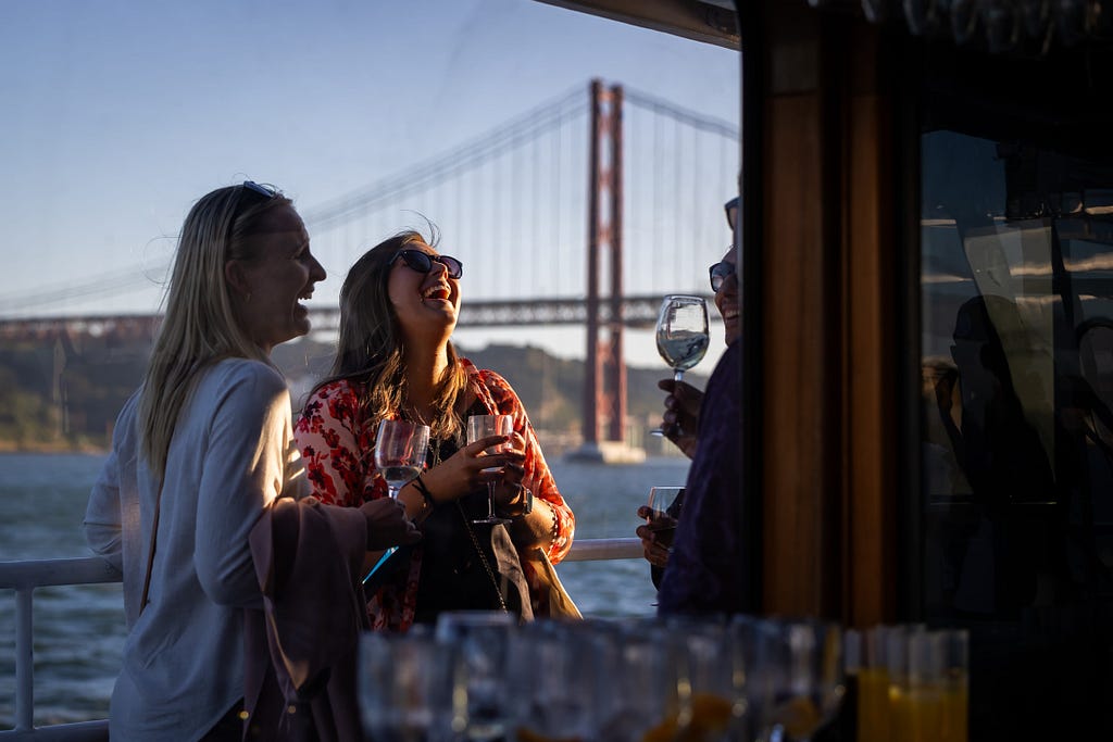 Attendees laughing while holding glasses of wine. 25 de Abril bridge on the background.