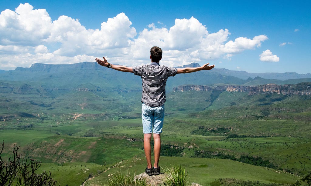 Man Standing in With Open Arms in Green Scenery