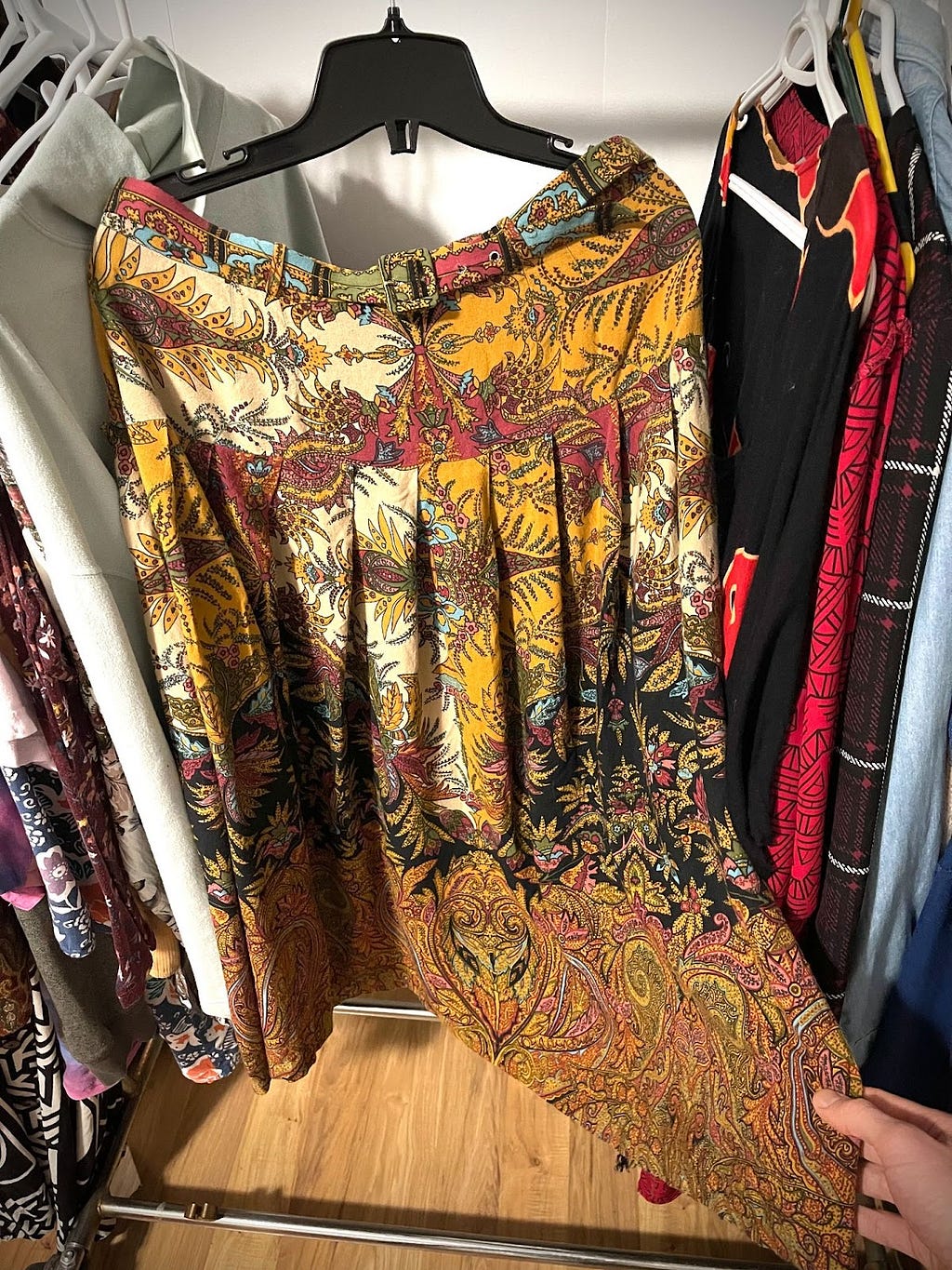 Long, thin skirt on clothing rack. Paisley patterns with orange, red, blue, cream, and black colours.