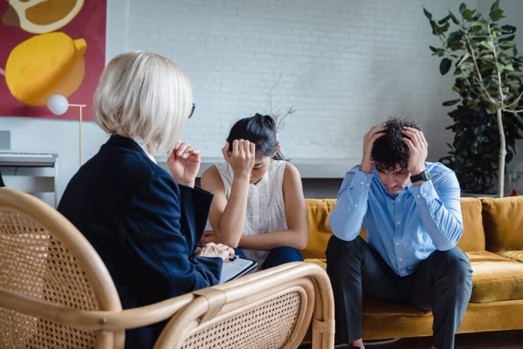 Two employees with their heads in their hands, sitting in front of their manager as they try to work out their conflict