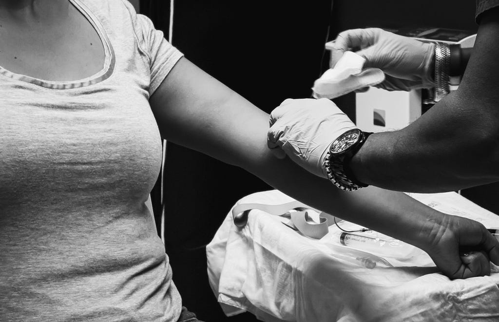 torso of woman getting blood drawn from her arm by a person wearing latex gloves