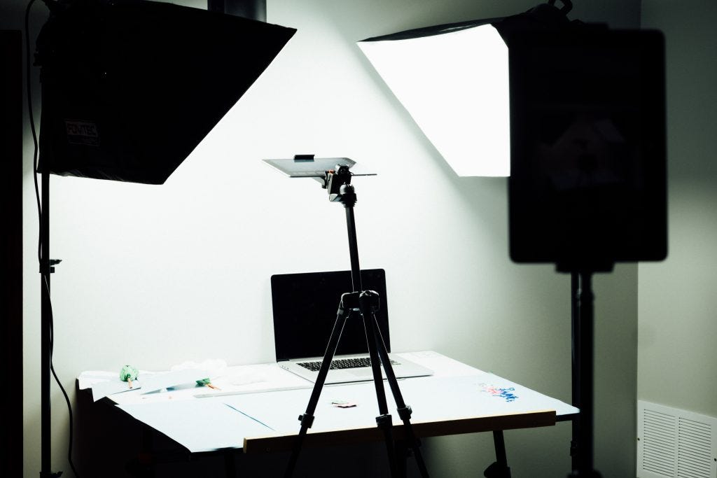 Laptop on a table surrounded by two studio lights. There is a white backdrop behind the table.