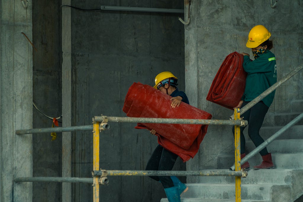 Two builders walking downstairs carrying equipment