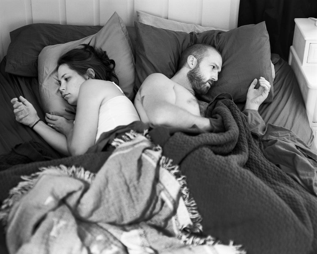 A couple in bed looking at their hands, where they’re supposed to hold their smartphone that have been removed