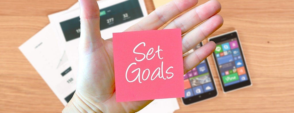 Person holding post-it note showing the words 'set goals'