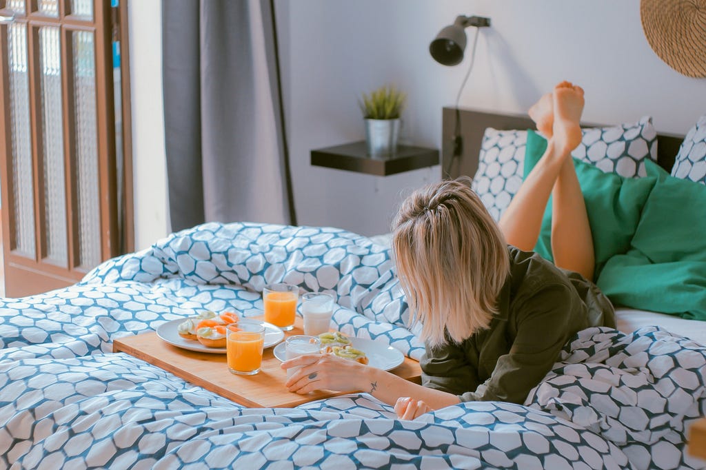 self-care: a woman on her bed with a tray of delicious food and orange juice