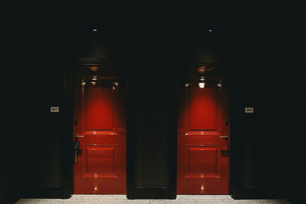Two red doors side to side illuminated against a black background.