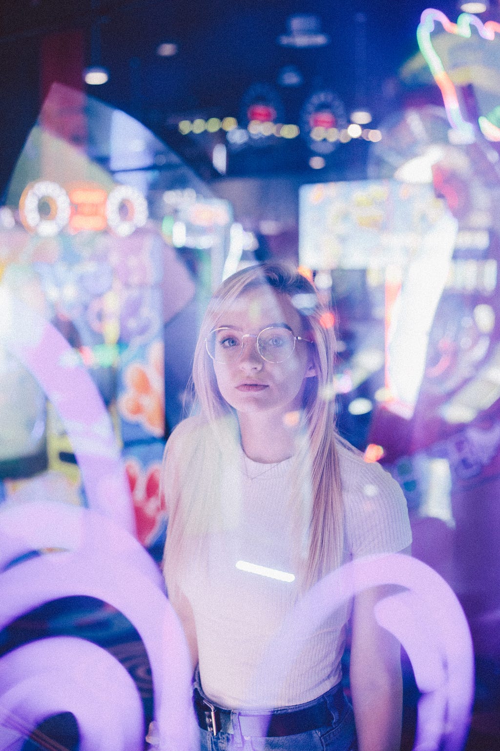 A woman standing behind glass. She is surrounding by colourful reflections and lights.
