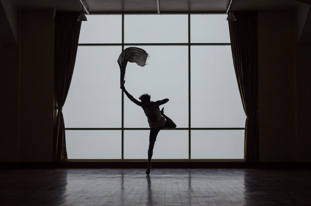A silhouette of a dancer, mid air, about to land on their right foot.