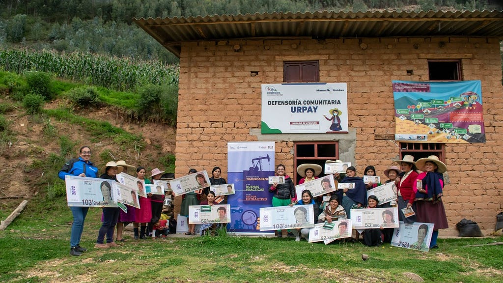 Women who are each holding posters of that represent royalty payouts pose for a group photo outside of a brick building.