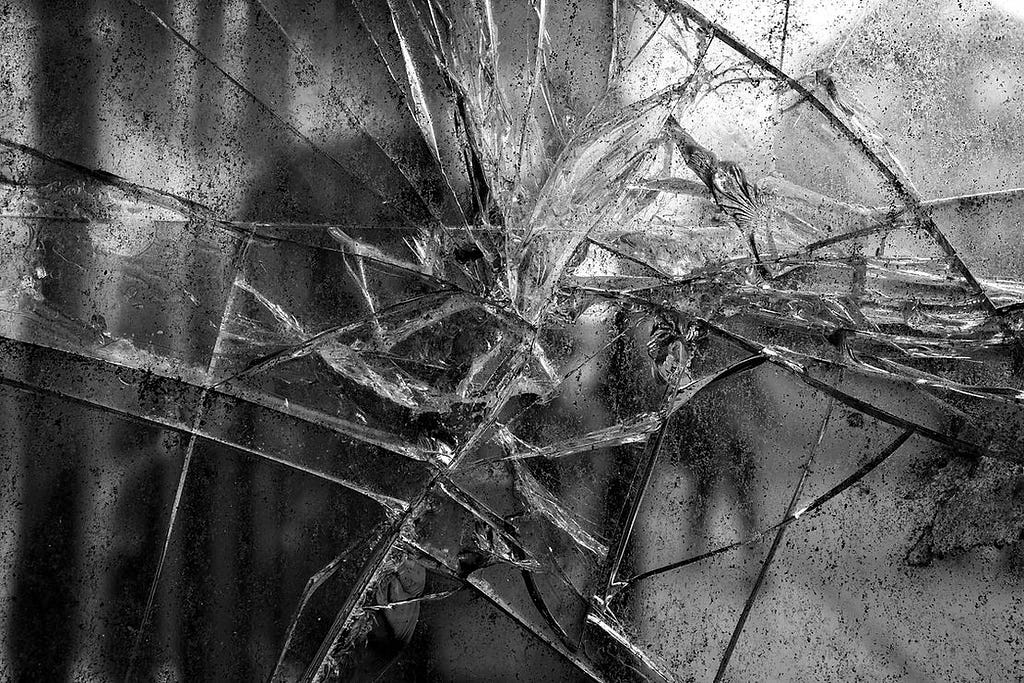 A black and white image of shattered glass or ice. The splintered lines serve as a metaphor for the way we are fractured as we move through life collecting trauma wounds.