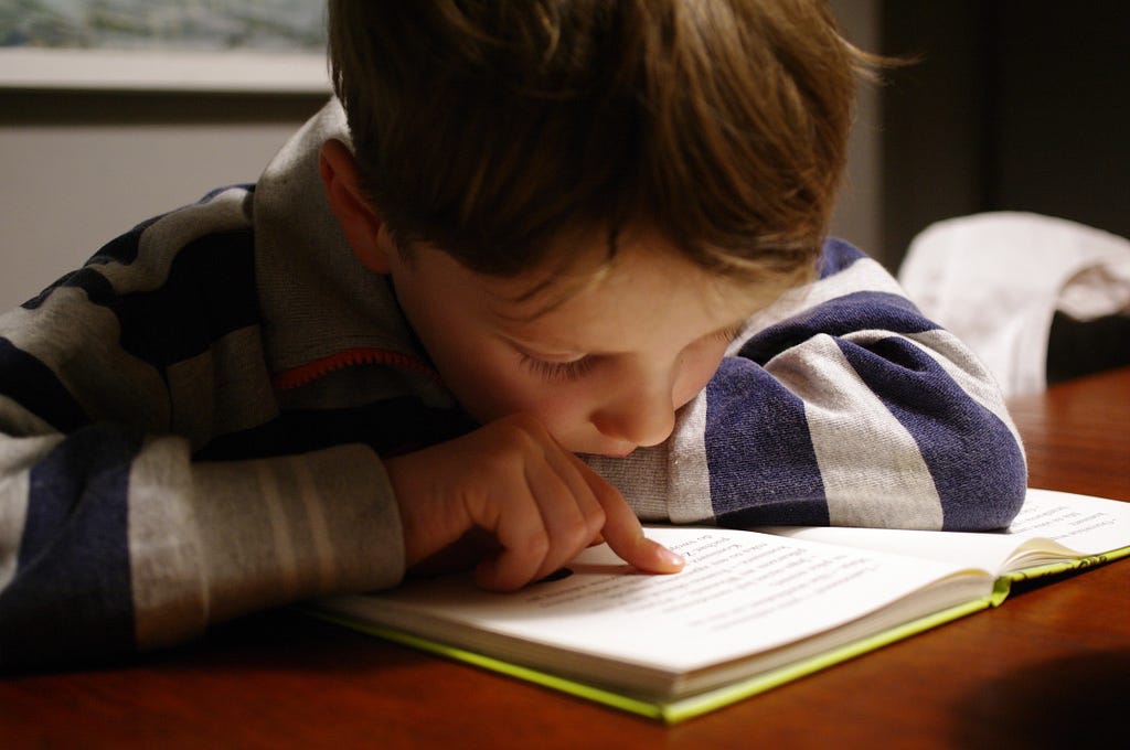 A young boy leant over a book reading at a table