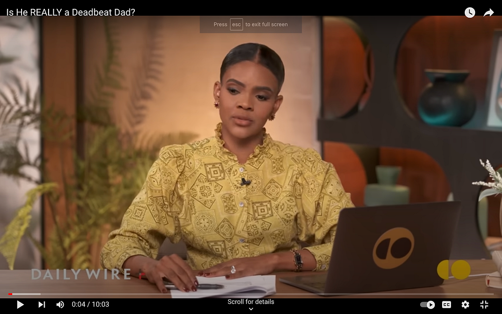 A screenshot from Candace Owens’s show on The Daily Wire. Her blouse is mustard yellow with what I’ll describe as a funky pattern of shapes and a ruffled collar.