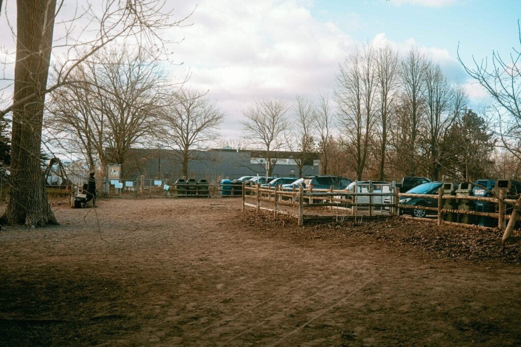 Two main entrances to Cherry Beach - taken from inside the dog park overlooking the nearby parking lot. On the sides are rows of green bins and disposal bins. Bins are facing both inwards and outwards to provide ease of access to dog owners coming in and leaving the park. 