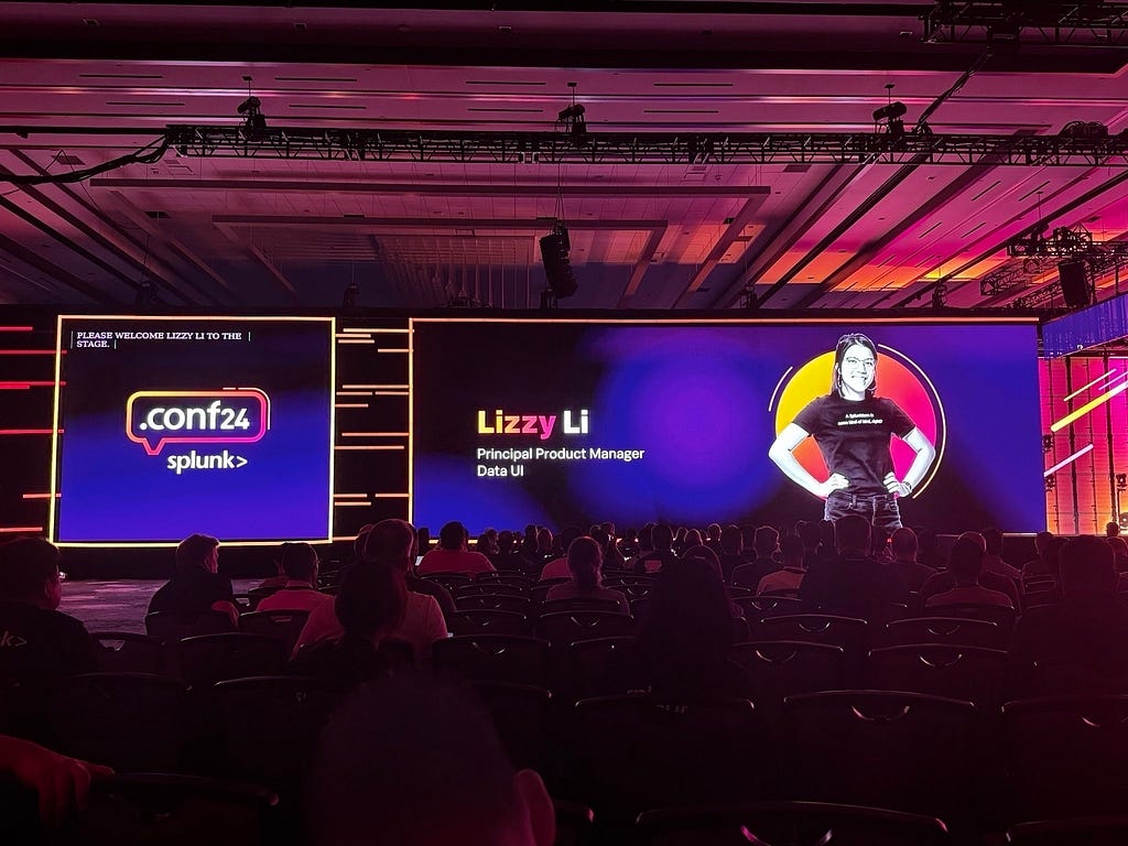 An audience watches a conference presentation featuring a large screen displaying a woman named Lizzy Li, identified as a Principal Product Manager from Splunk, standing on stage.