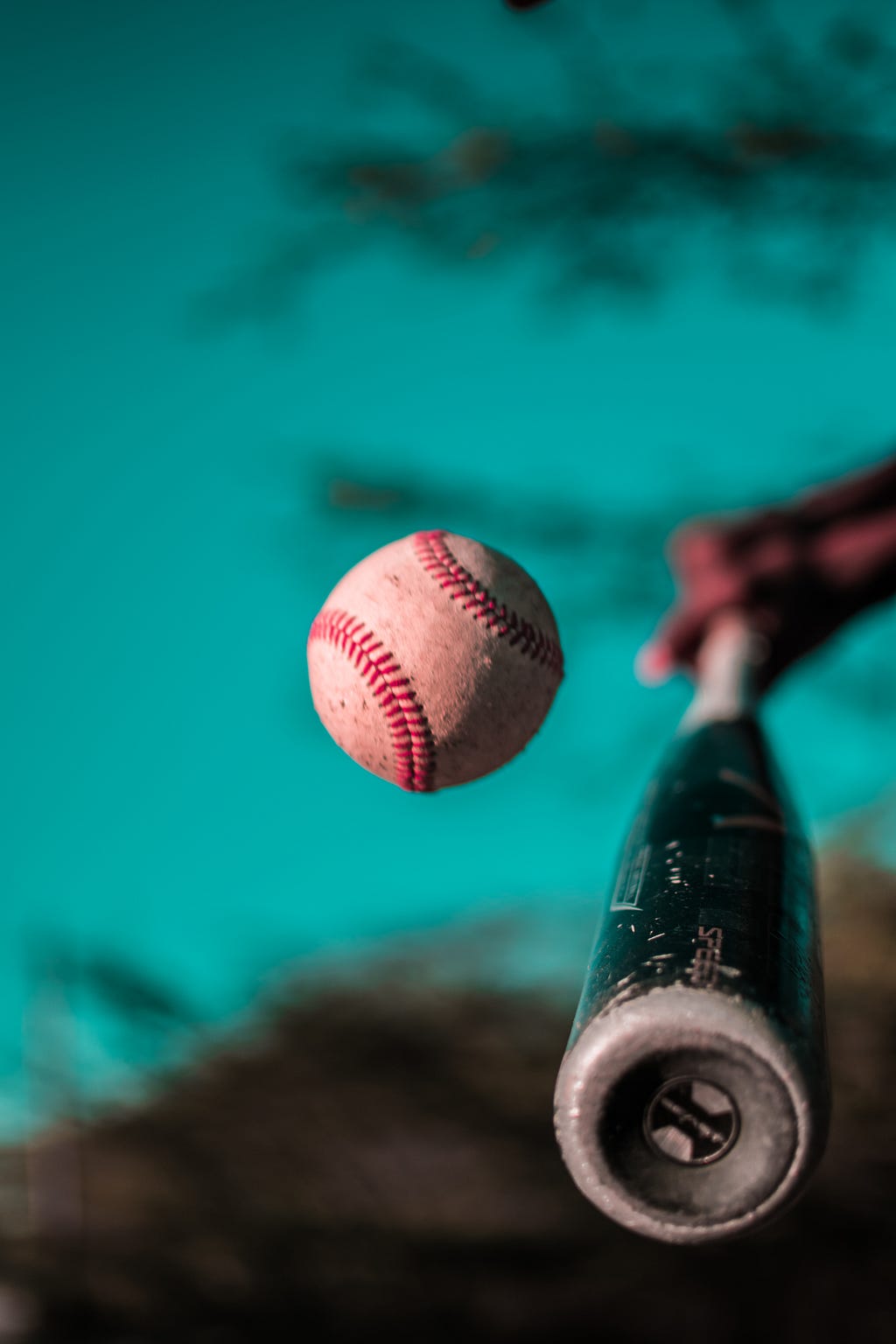 White baseball with red threading floats in front of black baseball bat on blue background.