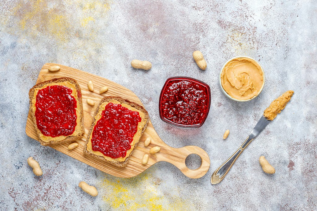 deconstructed pb&j sandwich on a cutting board next to jars of peanut butter and jelly