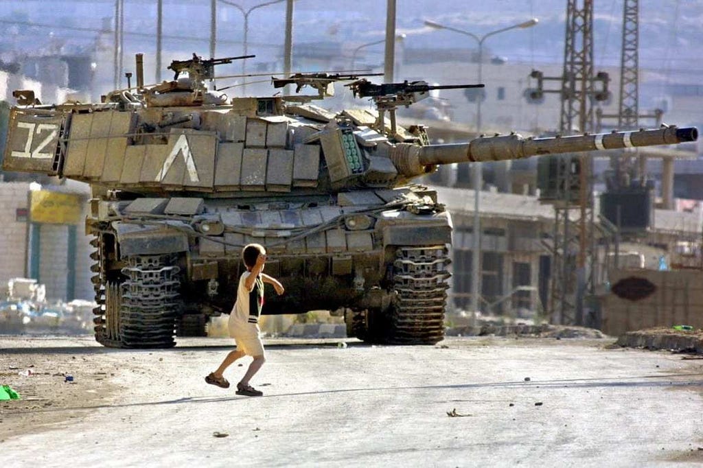 A boy stands in front of a huge tank, arm back to launch a stone