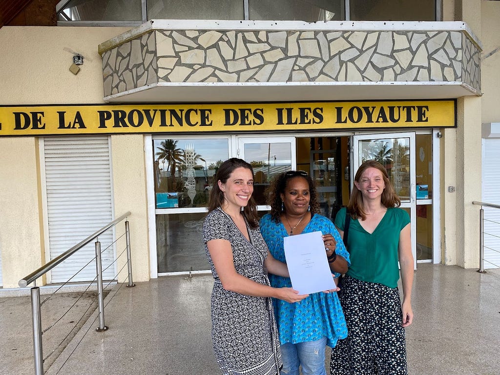 Sarah LeBaron von Baeyer from Variant Bio, Marie-Rose Waia from DACAS, and Stéphanie Fabre, the rheumatologist overseeing the study, holding a memorandum of understanding signed together in Drehu (Lifou).