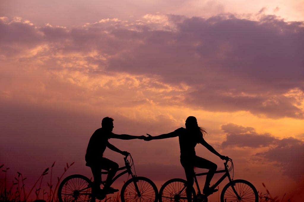 Two bicyclists holding hands while riding on separate bikes