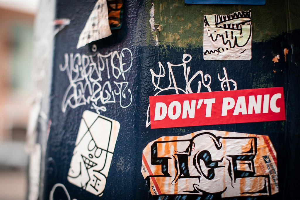 Stickers and graffiti on a wall. One says, “Don’t Panic.”