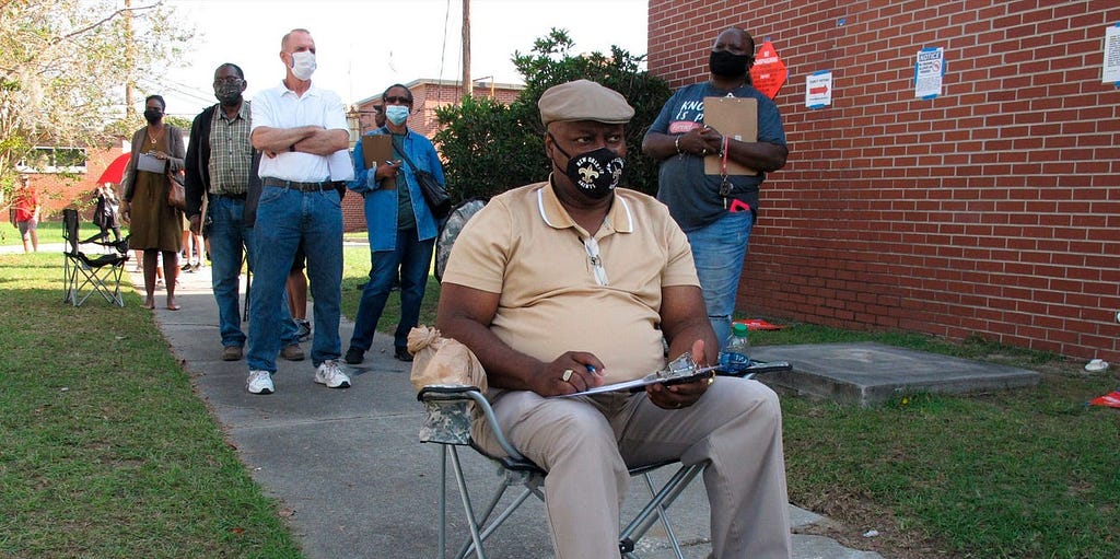 Richard Williams sits in a folding chair, filling out paperwork, as he waits in line to vote early in Savannah, Ga.