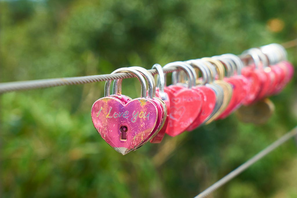Many small heart padlocks strung together across a metal wire fading into the distance.