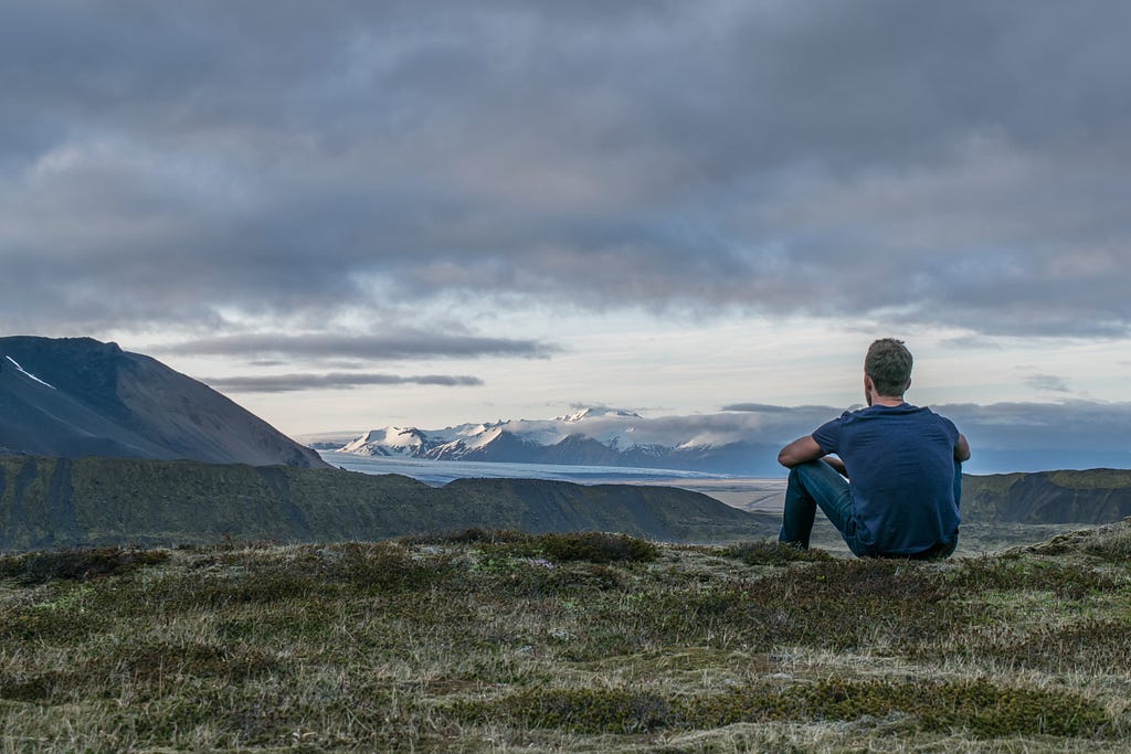 A man looking at a view of a mountain in England. White male on the grass